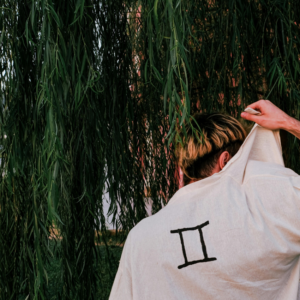A man holding up the back of his shirt which has the Gemini symbol on it to represent the Moon in Gemini energy.