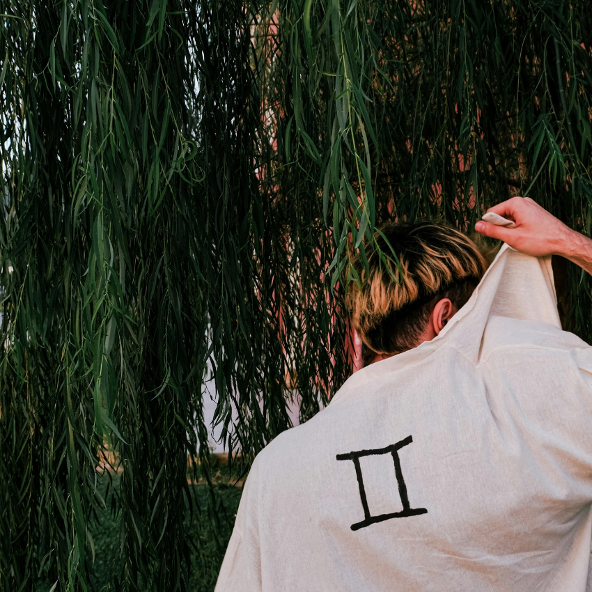 A man holding up the back of his shirt which has the Gemini symbol on it to represent the Moon in Gemini energy.