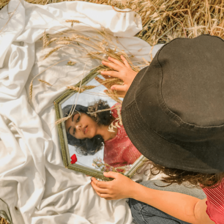 A woman looks down into a hexagonal-shaped mirror, her reflection representing the astrological energy of the week.