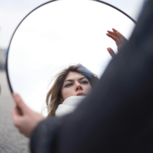 A woman looks into a mirror, representing the astrological reflection to do this week.