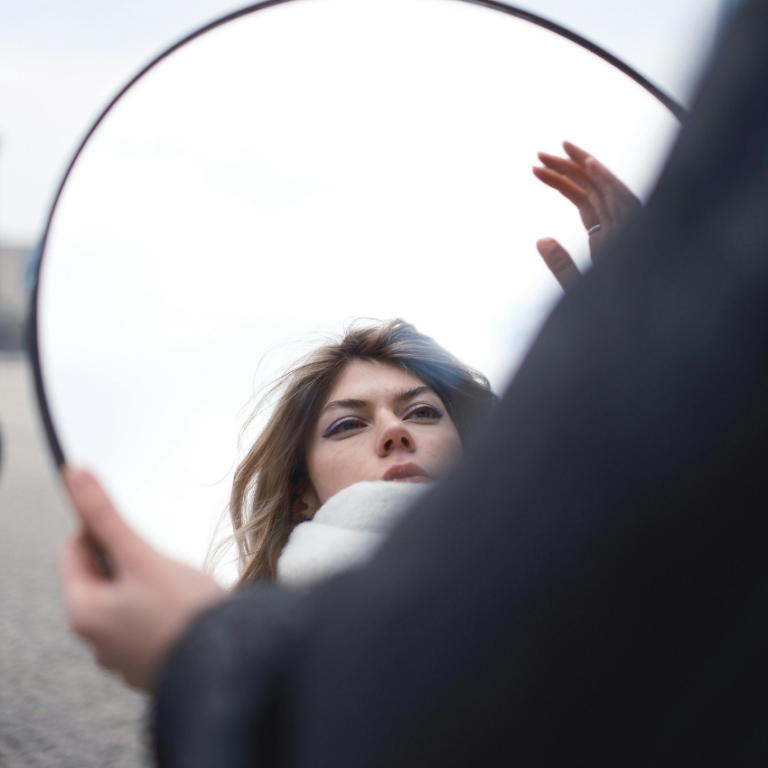 A woman looks into a mirror, representing the astrological reflection to do this week.