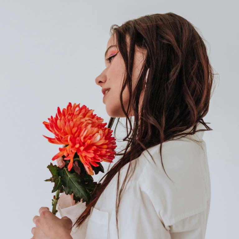 A woman with long brown hair holds a vibrant orange flower, representing the energy of April.