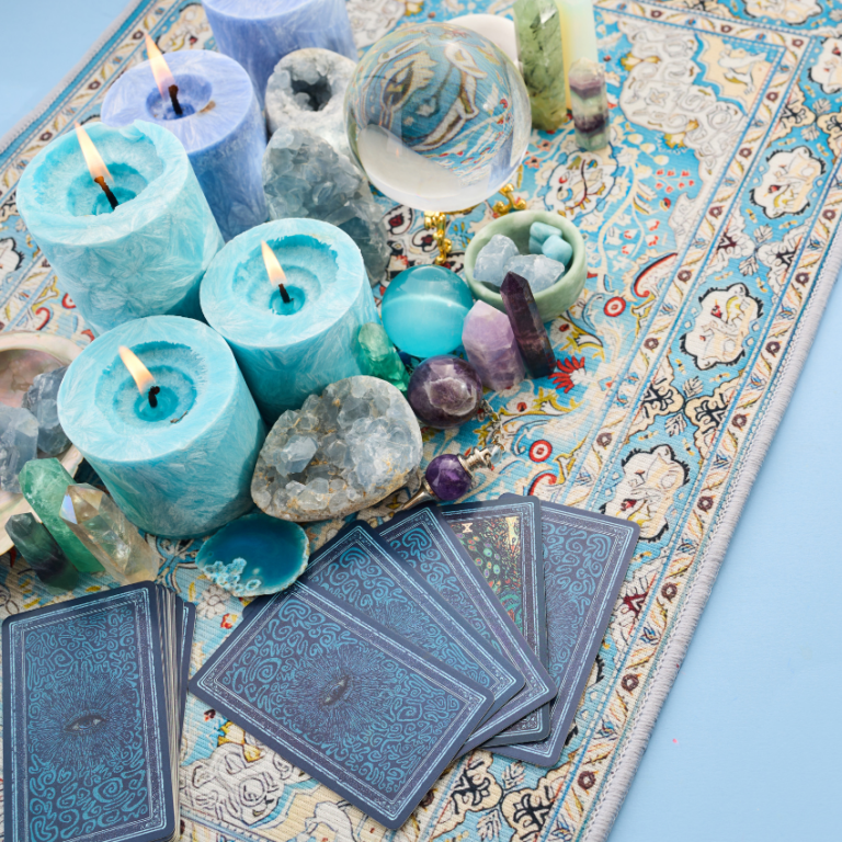 Tourquoise candles are lit on a patterned runner with face-down Tarot cards to represent the energy of April Tarot horoscopes.