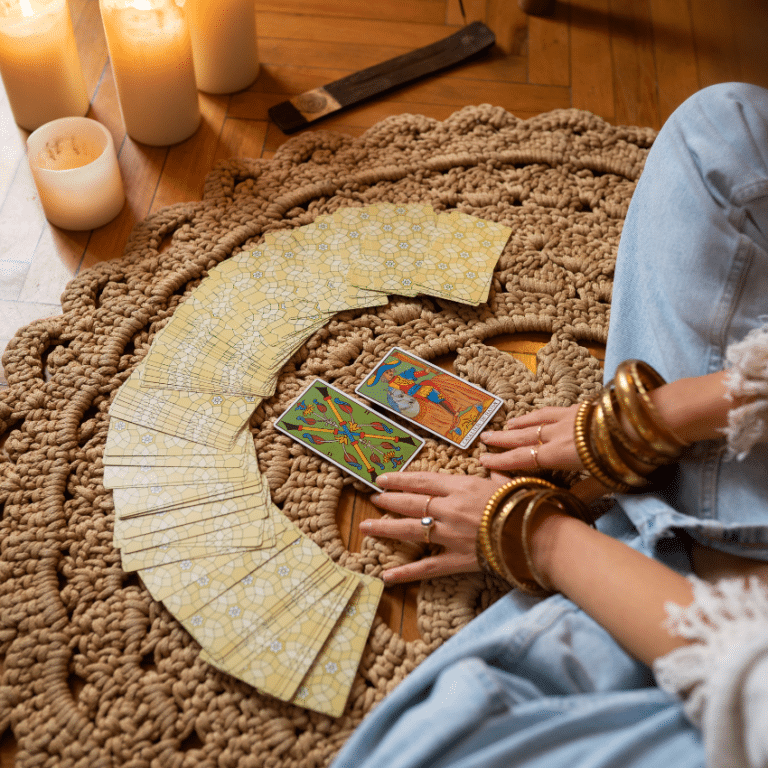 A fan of Tarot cards face down with a person sitting cross-legged in front of them. There are lit candles to represent the energy of March 2026 Tarot horoscopes.