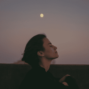 A woman with short brown hair with her eyes closed under a Full Moon in the distance to represent the Moon in Sagittarius.