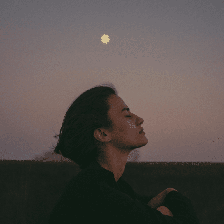 A woman with short brown hair with her eyes closed under a Full Moon in the distance to represent the Moon in Sagittarius.