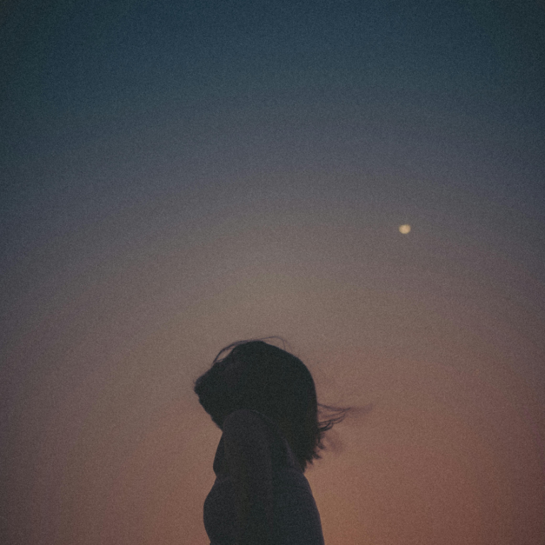 The outline of a person against a dusky colored sky with the Moon visible in the background to represent the energy of the Moon in Taurus.