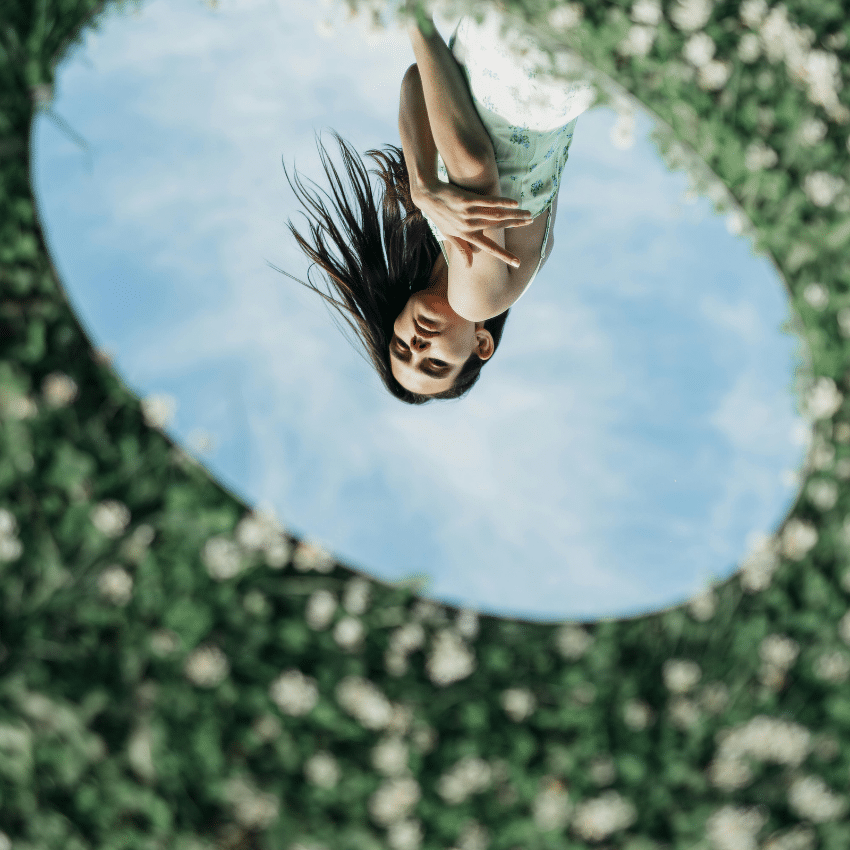 A woman's reflection in a mirror upside down. The mirror is in a field of flowers to represent the energy of spring 2026.