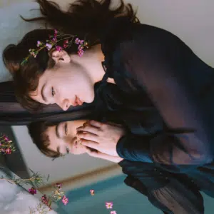 A woman lays on a mirror, reflecting her face at peace.