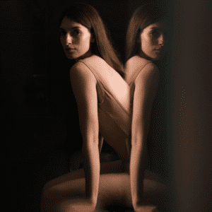 A woman sits in front of a mirror, her reflection visible to reflect the energy of this week's astrology.