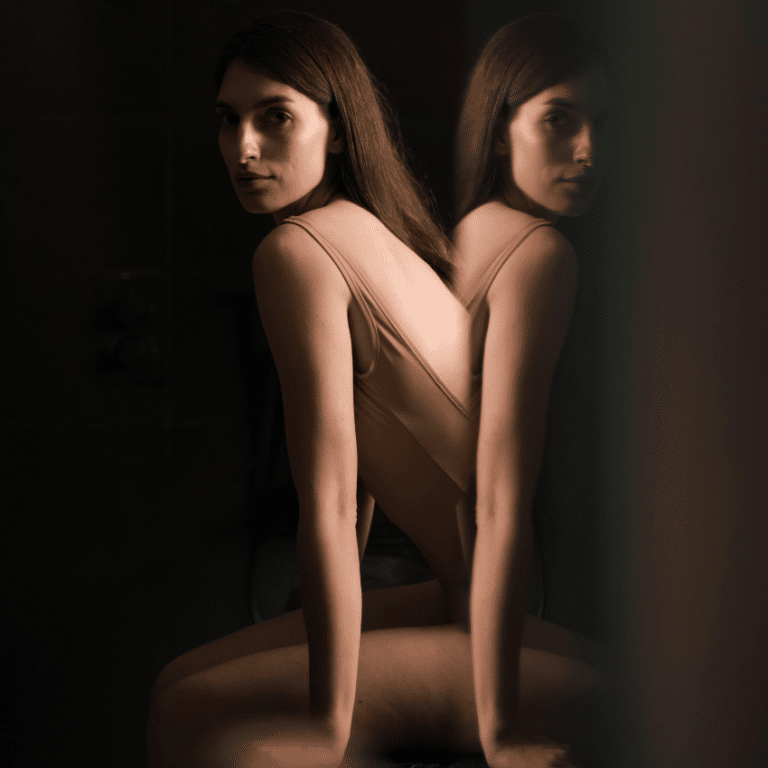 A woman sits in front of a mirror, her reflection visible to reflect the energy of this week's astrology.