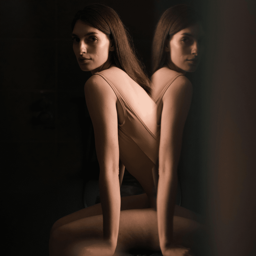 A woman sits in front of a mirror, her reflection visible to reflect the energy of this week's astrology.