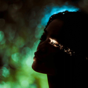 A woman is backlit by green and blue light. The only visible part of her face is her eye, representing the energy of the Aries New Moon.