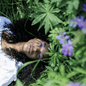 A black woman lays underneath purple flowers with green leaves, representing the astrological energy of May 2026.