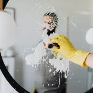 A person smears soap on a mirror, hiding their reflection, but revealing their bright yellow rubber glove.