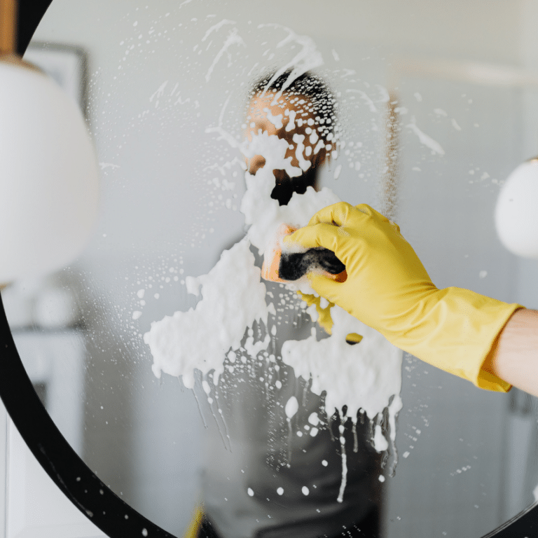 A person smears soap on a mirror, hiding their reflection, but revealing their bright yellow rubber glove.