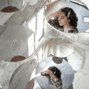 A woman's reflection in two mirrors is shown on the ground surrounded by bright light.