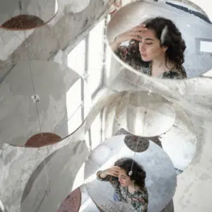 A woman's reflection in two mirrors is shown on the ground surrounded by bright light.