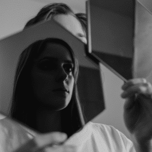A woman holds up a mirror, reflecting her image back to the viewer.