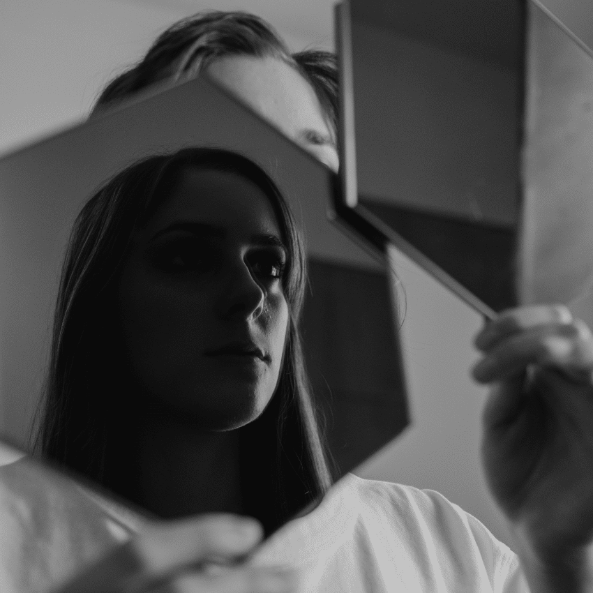 A woman holds up a mirror, reflecting her image back to the viewer.