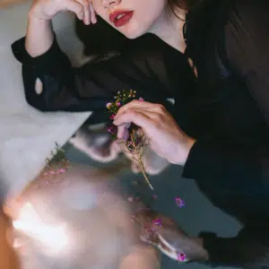 A woman's face next to a mirror, reflecting back a pool of light and her lips.