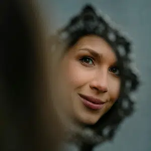 A woman's reflection is seen in a small but ornate handheld mirror.