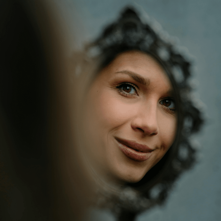 A woman's reflection is seen in a small but ornate handheld mirror.