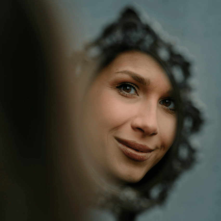 A woman's reflection is seen in a small but ornate handheld mirror.